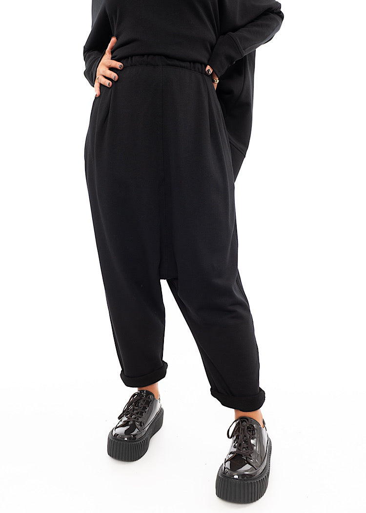 A Model wearing a Black fitted Trouser with a semi rolled up ankle. Featuring slight seam details along the elasticised waistband.