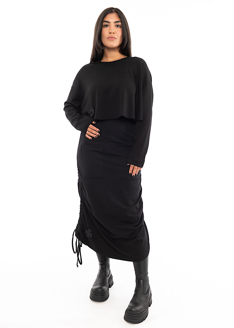 A full frame photo of A Model wearing a Black drawstring Skirt, styled with a cropped Black Pullover and Chunky Black Boot.