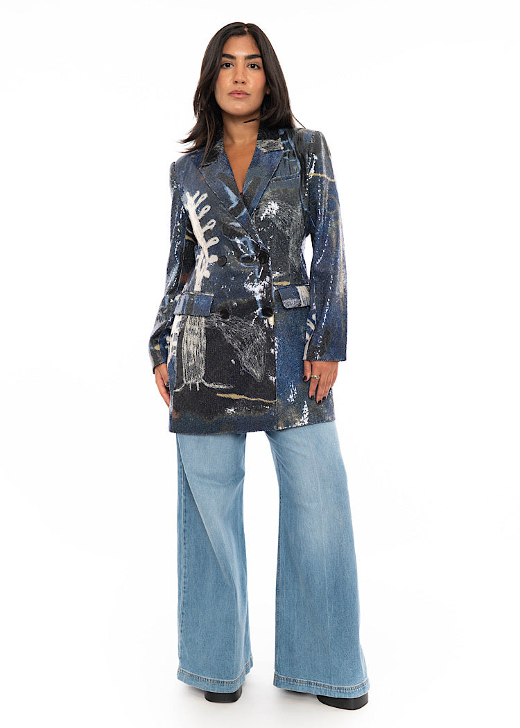 A model wearing a Blue and Black Sequin Blazer. With two front pockets and buttons to fasten. Styled with light blue straight leg jeans and black high heels.