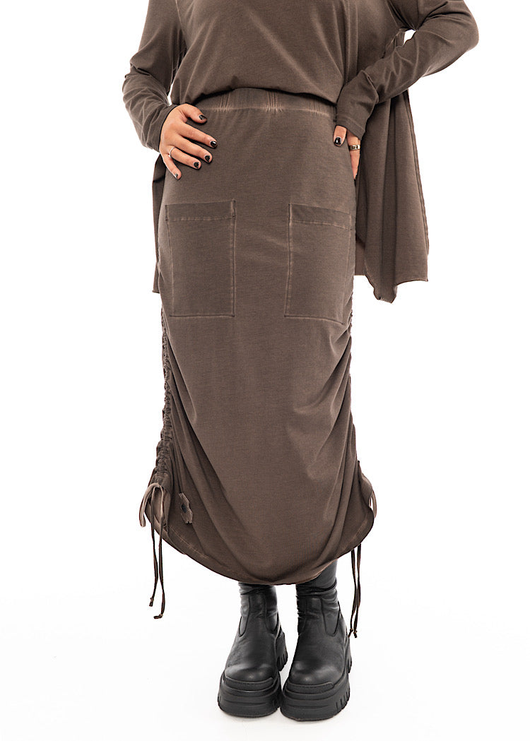 A Model wearing a Chocolate Brown skirt with two front square pockets and two dramatic tied drawstrings which give it a rouging effect. Styled with matching Brown pullover and Black boot.