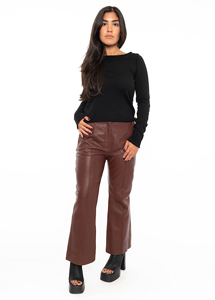 Model wearing cropped, flared Burgundy leather trousers with a black fitted pullover with a seam detail down the centre of the leg. Styled with Black high heels.