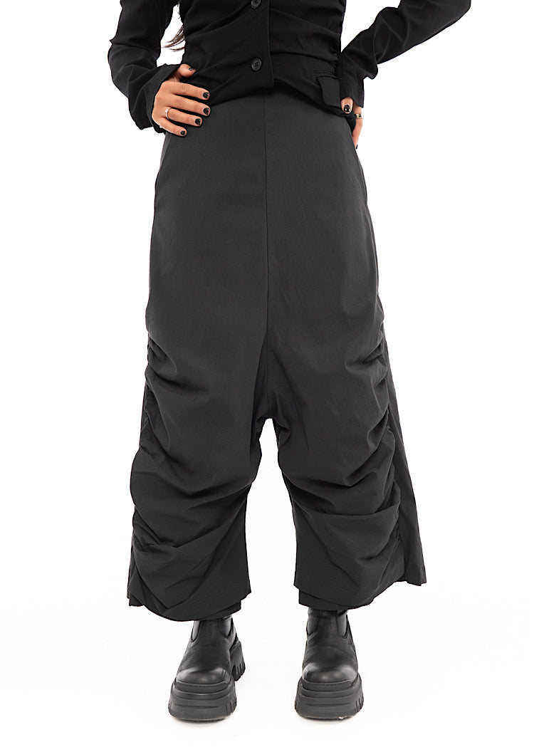A Model wearing a drop-crotch Trouser in a washed dark Grey colour. With a kick-flare leg and structured leg designs.