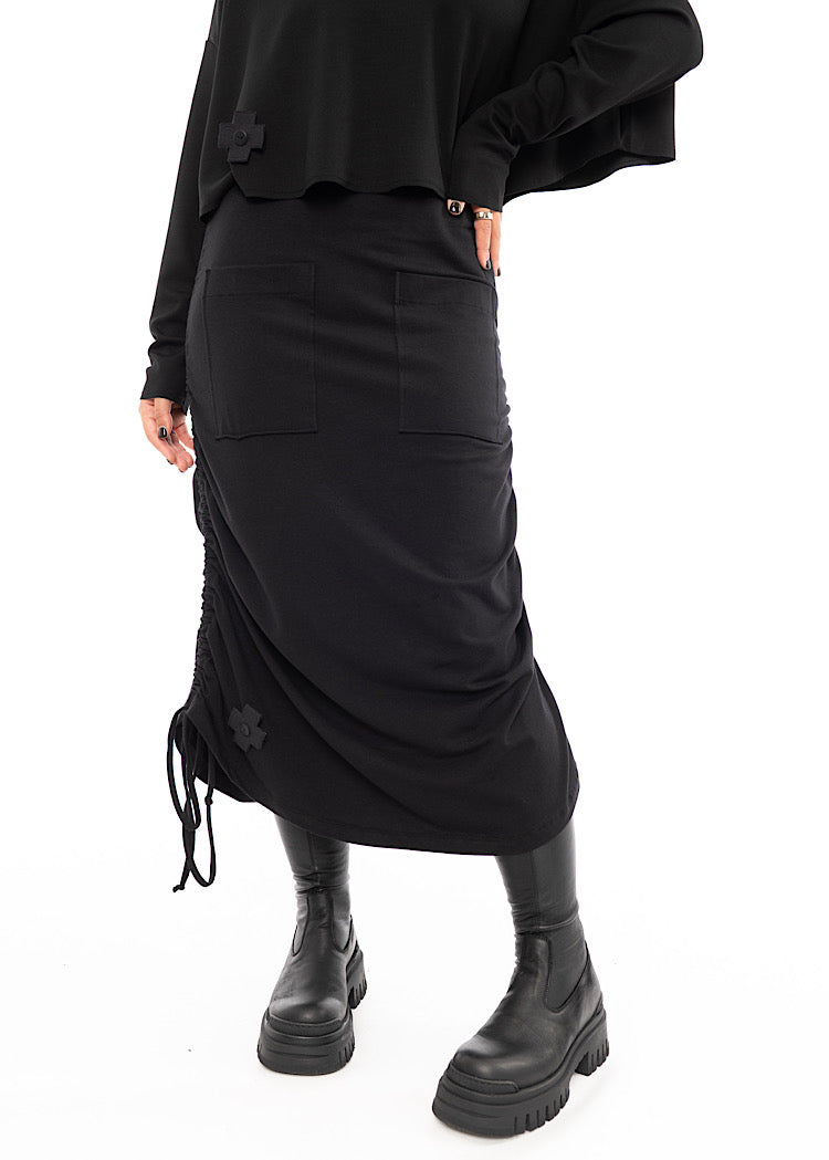 A Model wearing a Black drawstring Skirt, styled with a cropped Black Pullover and Chunky Black Boot. Showing the rouging style on the skirt.