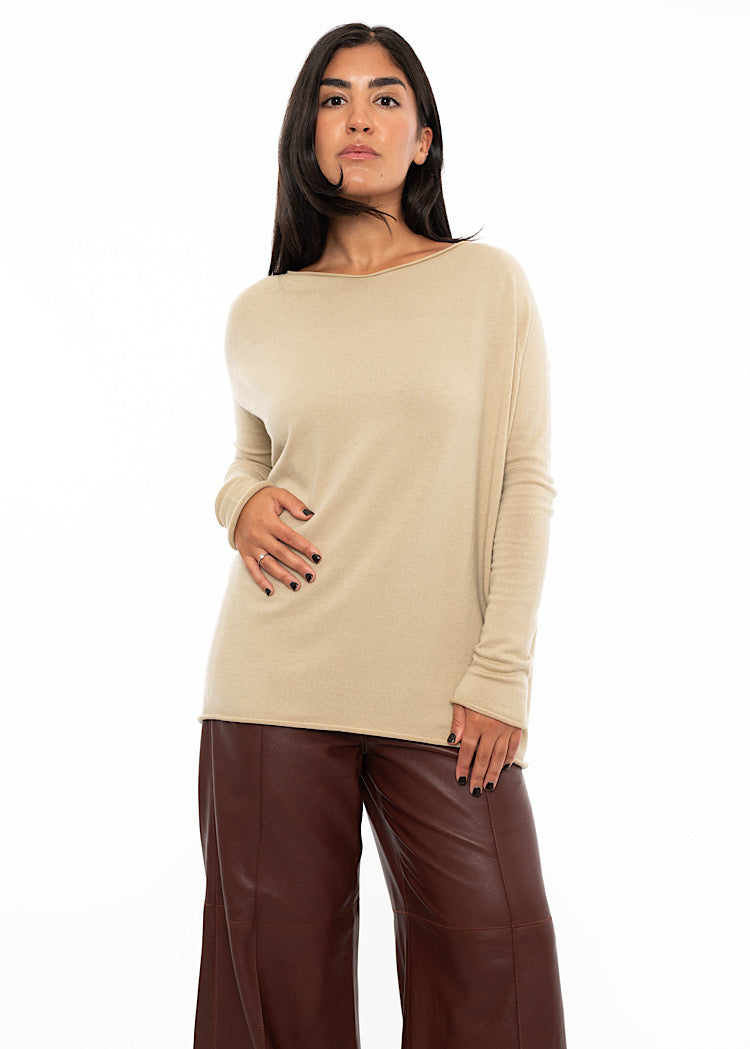 A Model wearing a relaxed fit beige pullover with a slash neckline and long sleeves, finishing at the hip. Styled with burgundy wide leg leather trousers.