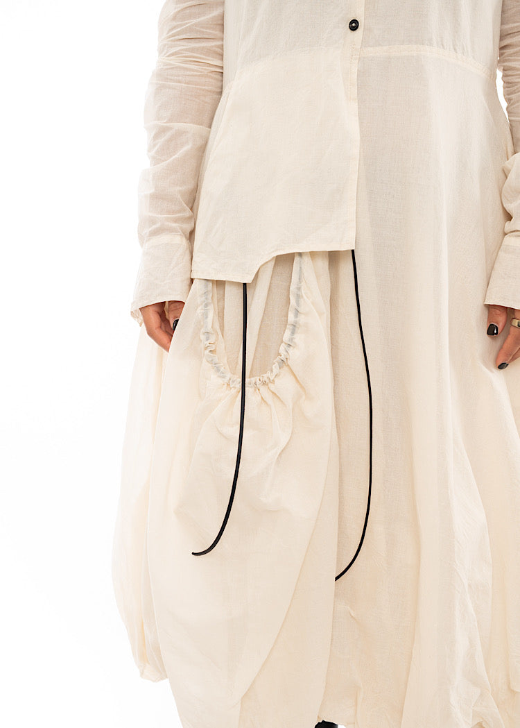 An up close off A Model wearing a bubble skirted Dress in a creme colour. Focusing on the flap pocket and Black string pieces.