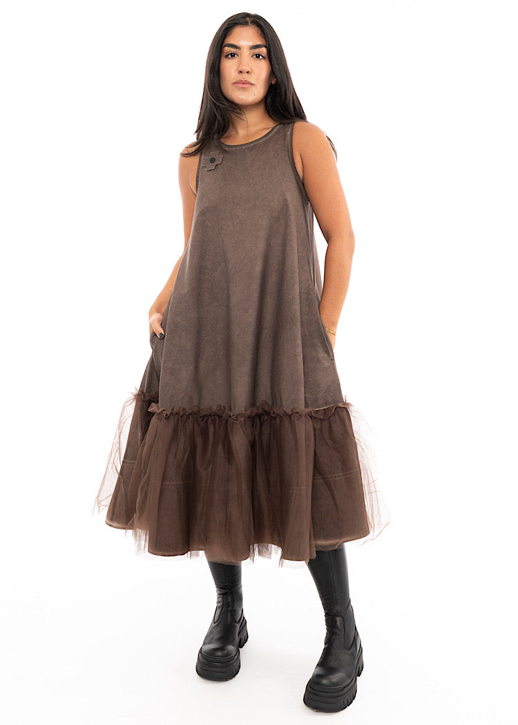 A Model wearing a Chocolate Brown sleeveless A-line dress with a mesh layer close to the hem of the dress.Styled with a chunky black boot.