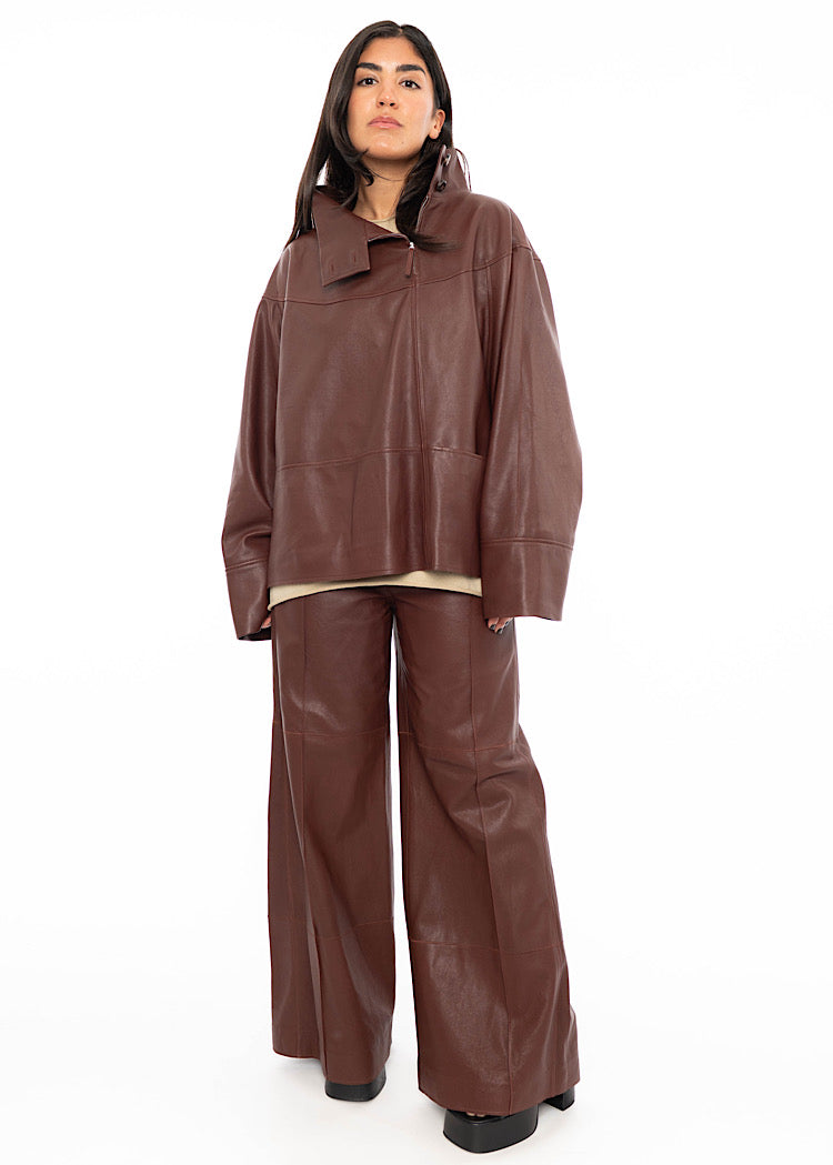 A model wearing an oversized Burgundy Leather pullover with relaxed fit sleeves with a beige pullover underneath. Styled with wide leg trousers in the matching Burgundy leather and black high heels.