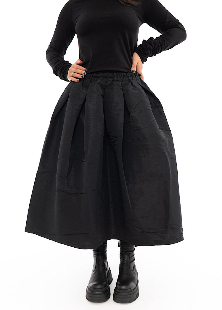 A Model wearing a Black Structured Skirt, paired with a matching Black Top and Chunky Boots. Showing the top tucked into the Skirts waistband, disclosing different styling techniques.