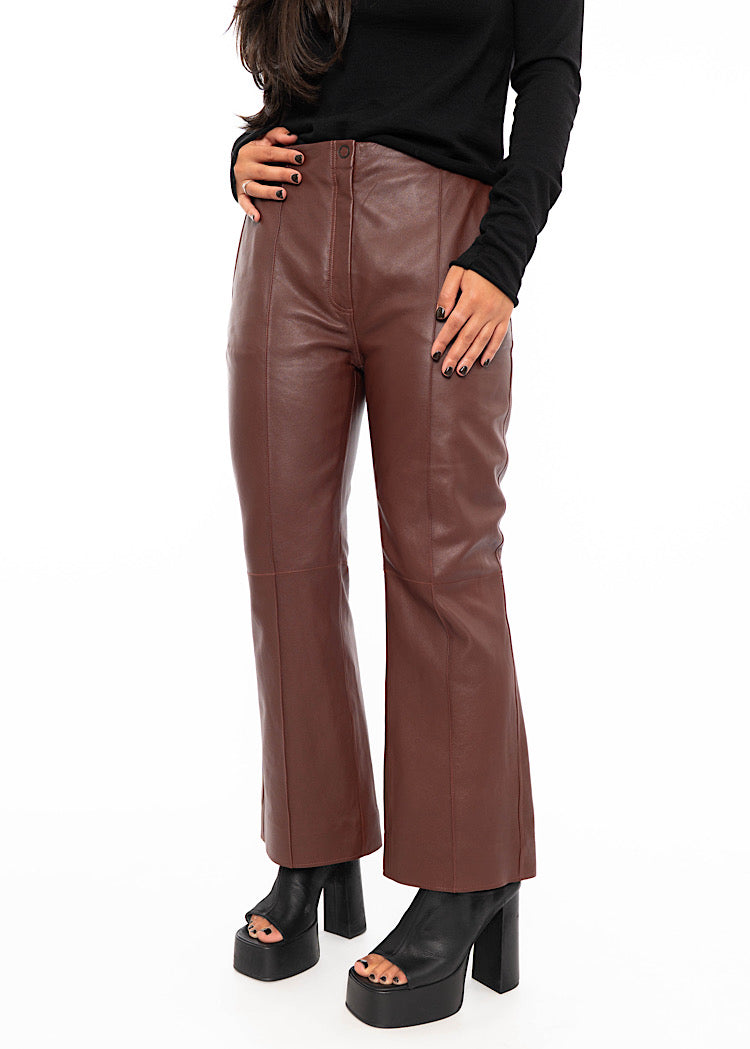 Model wearing cropped, flared Burgundy leather trouser with a black fitted pullover. Focusing on leather trousers leg length and minimal details.