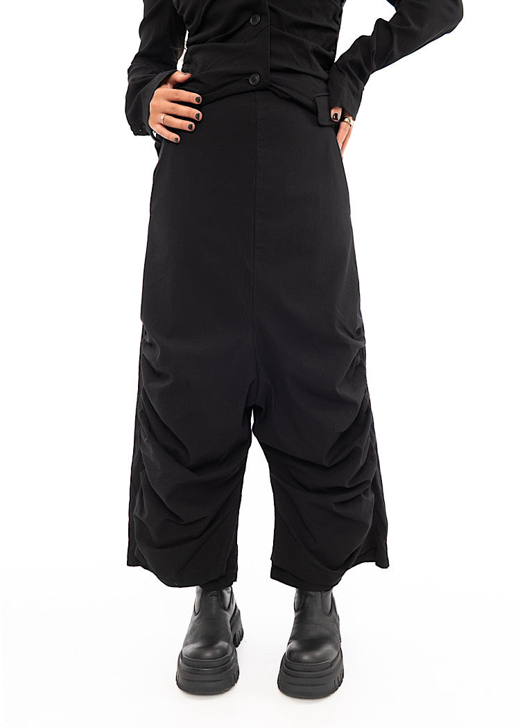 A Model wearing a drop-crotch Trouser in a Black colour. With a kick-flare leg, paired with Chunky soled Black Boots.