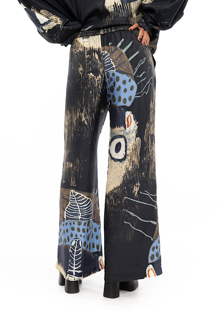 A close up off a model wearing a wide leg Silk trousers. Standing facing the back, showing the abstract design from behind.