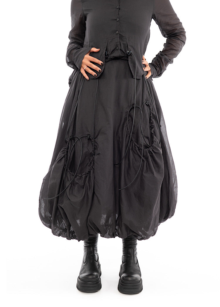 An up close photo of A Model wearing a bubble skirt, in a Grey colour. Focusing on the Black string details and pockets. Styled with Black Boots.