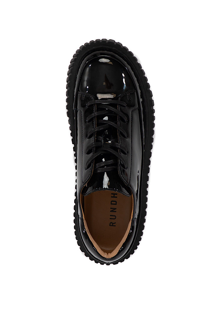 A picture from above of a Black glossy patent leather Shoe. Showing the matching Chunky Sole. Finishing with a classic lace up detail.