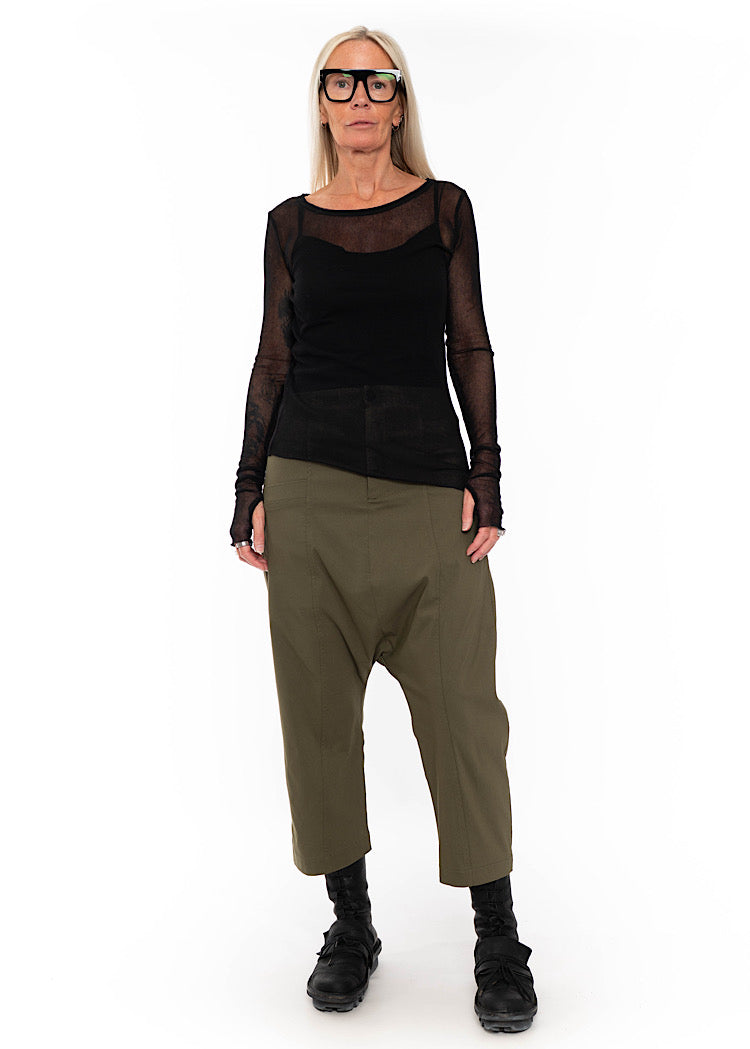 Model wearing black sheer mesh long-sleeve top with olive green drop-crotch cropped trousers and black combat boots.