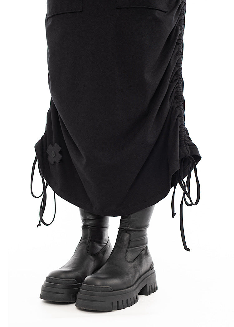 An up close of A Model wearing a Black drawstring Skirt, styled with a Chunky Black Boot. Showing the bottom of the skirt.