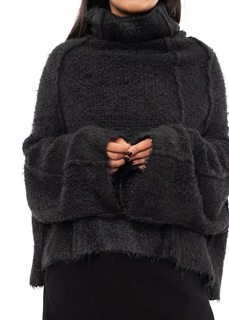 An up close of A Model wearing a Fluffy Dark Grey Pullover. Showing the structural lines and width of the sleeves.