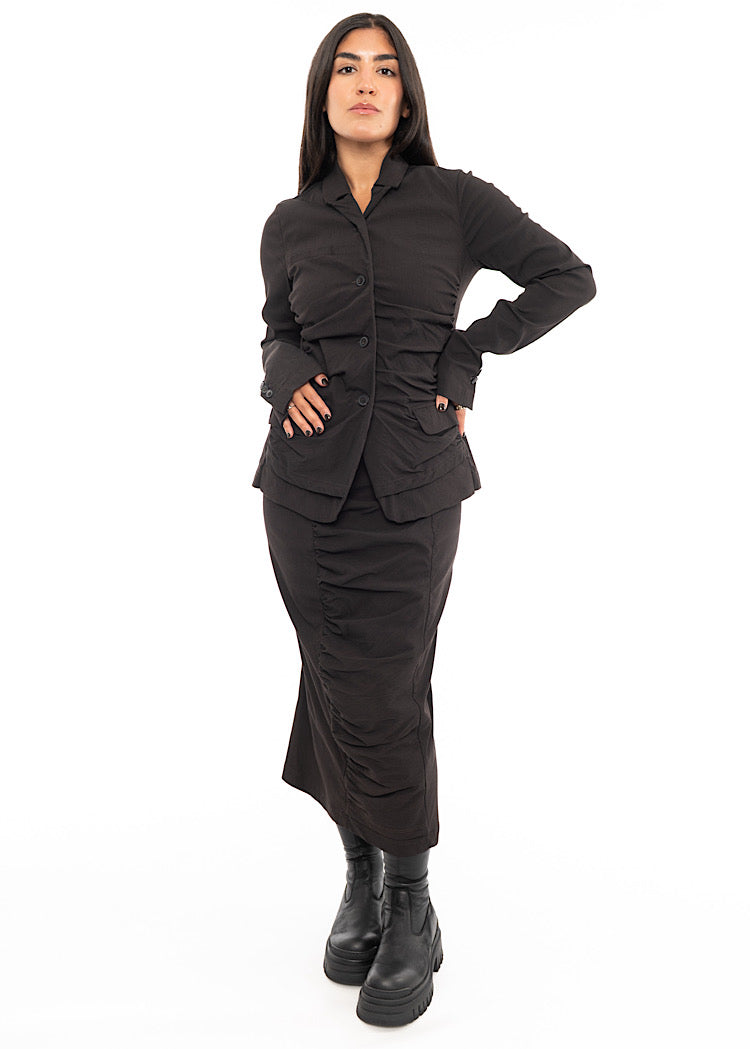 A full frame photo of A Model wearing a fitted washed Brown Skirt, paired with a matching Jacket and Black Chunky soled Boots.