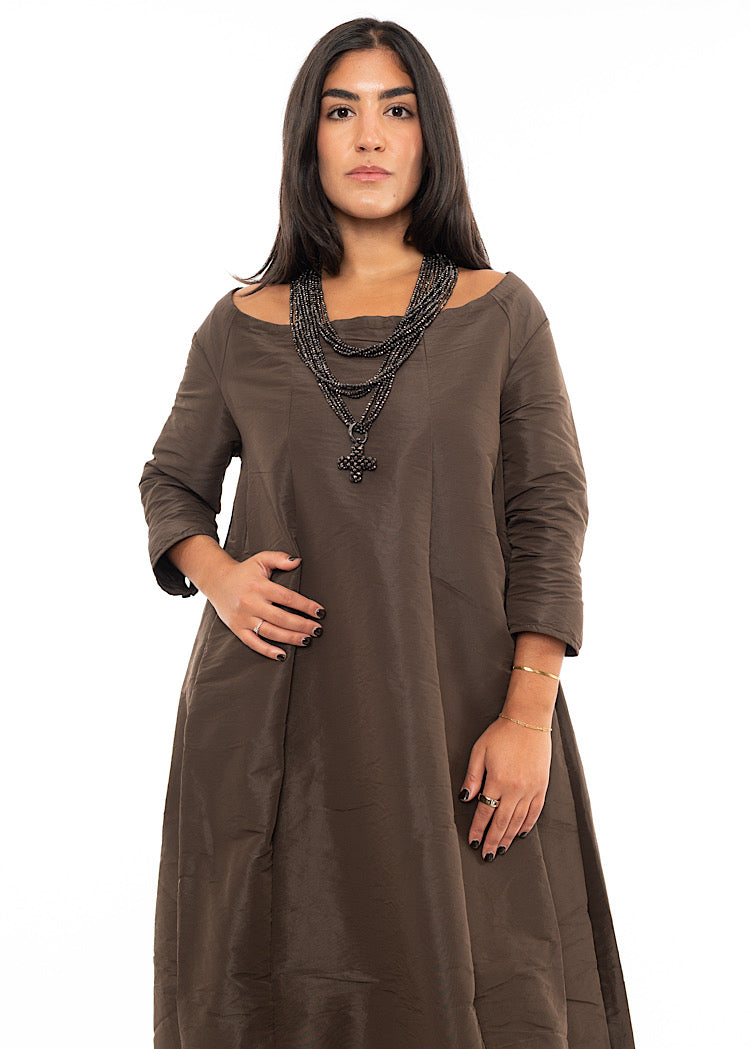 A Model wearing a triple layered circular beaded chain with a pendent and clasps too close.Styled with a Chocolate Brown dress with short sleeves.