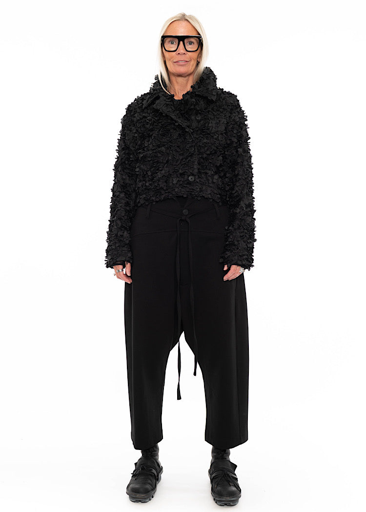 Model wearing black drop-crotch trousers with wide leg and drawstring detail, styled with mesh-sleeve top and combat boots. Also styled with a cropped button up jacket with 3d leaves