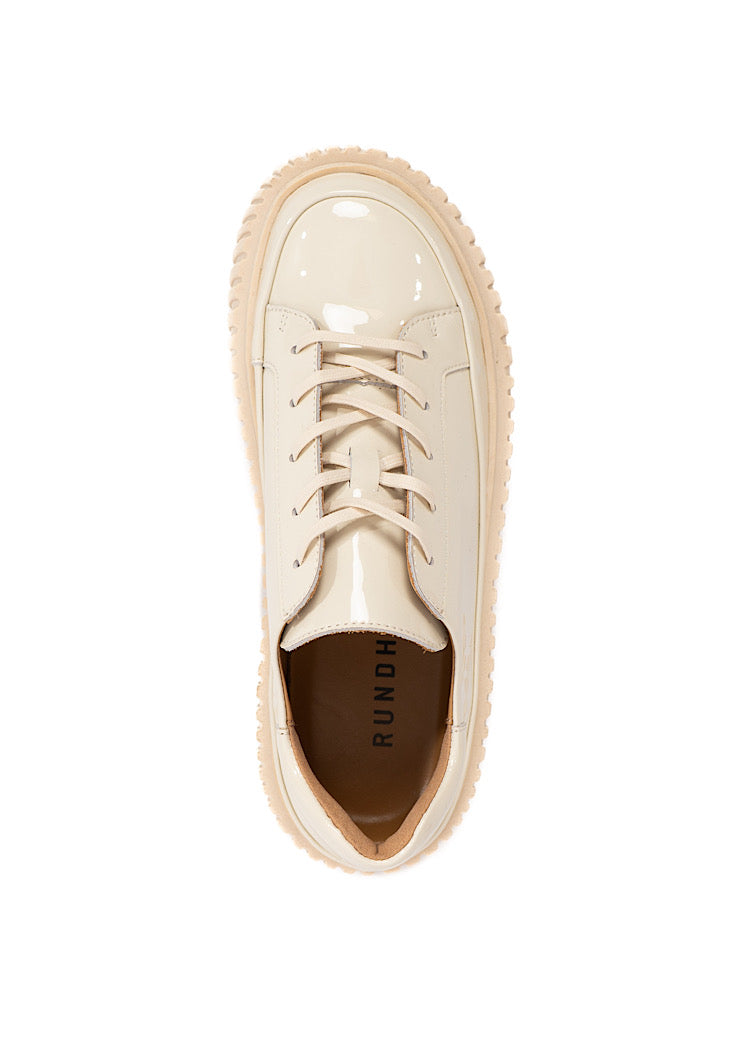 A picture from above of a Beige glossy patent leather Shoe. Showing the classic laced up design and the chunky sole from a different angle.