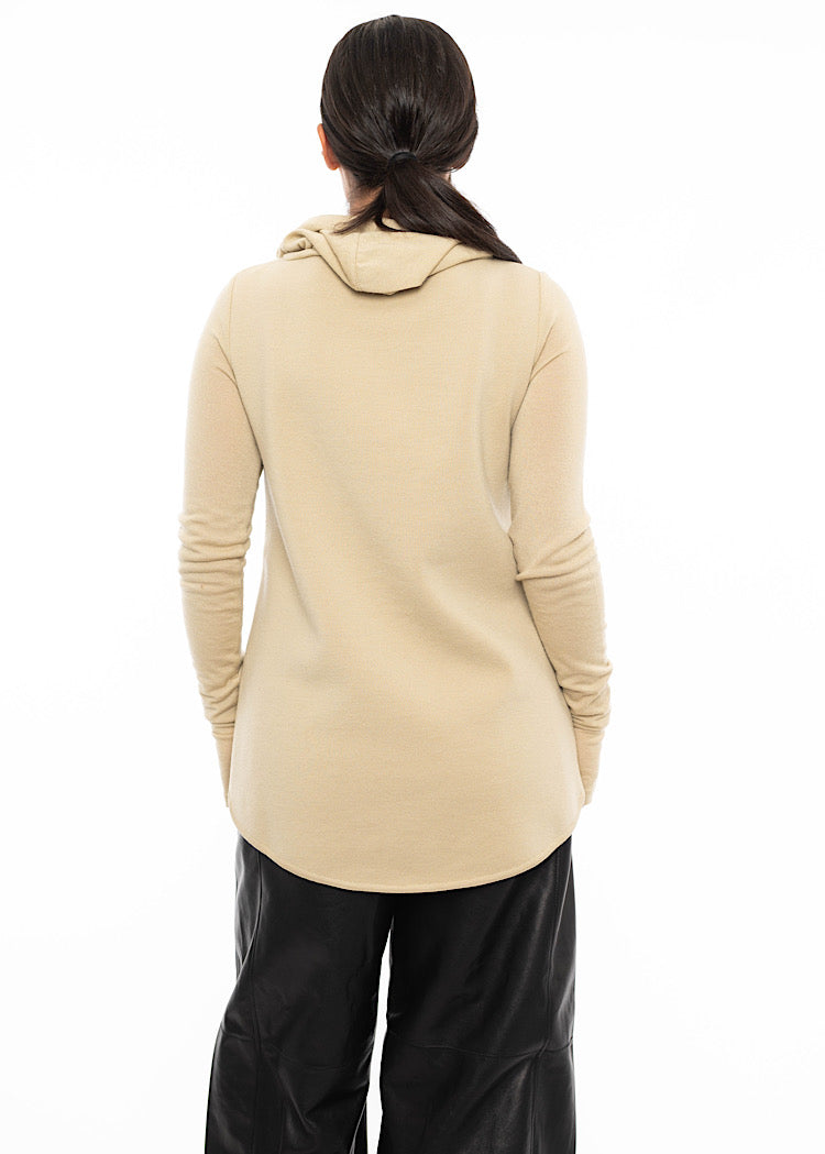 A model wearing a fitted warm beige pullover standing facing the back. Showing the hood on the piece and the long back length.