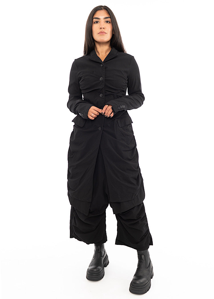 A full frame photo of A Model wearing a detailed techno coat and matching trousers, in a Black colour. Paired with a chunky Boot.