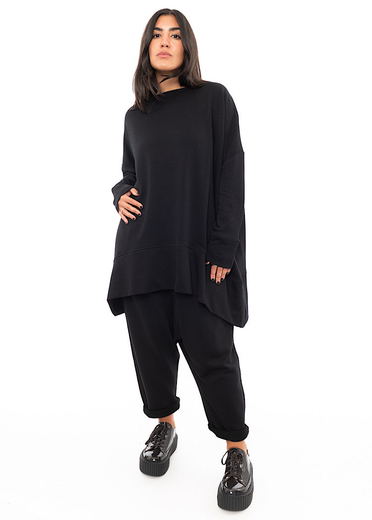 A Full frame photo of A Model wearing a Black Oversized Pullover. Paired with a matching Trouser and Brown Patent shoe.
