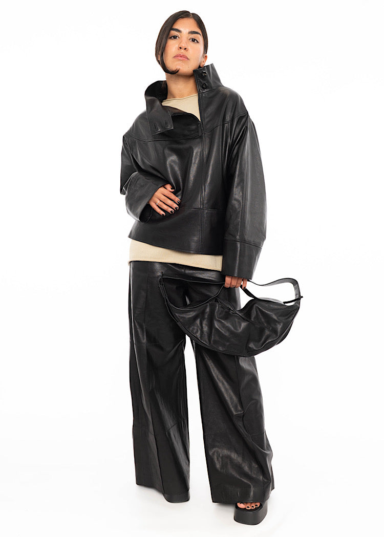 Model wearing Black Slouchy leather bag with a long strap and a shorter strap. Styled with a black Leather jacket, with black Leather straight leg trouser and beige pullover.