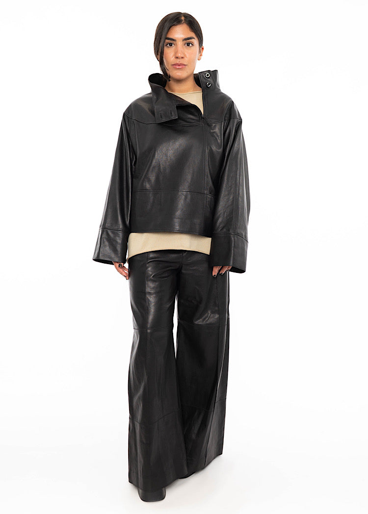 A model wearing an oversized Black Leather pullover with relaxed fit sleeves with a beige pullover underneath. Styled with wide leg trousers in the matching Black leather and black high heels