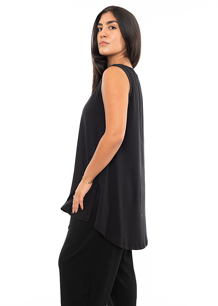 A Model standing to the side wearing a fitted Black Top with slits up the side, sleeveless design. Showing the width and length of the top.