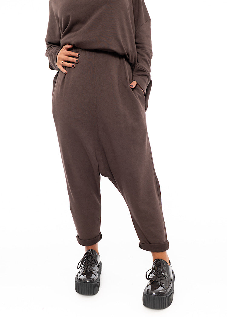 A Model wearing a plum toned drop-crotch trouser with a slight rolled up effect on the Ankle.Disclosing the pockets.