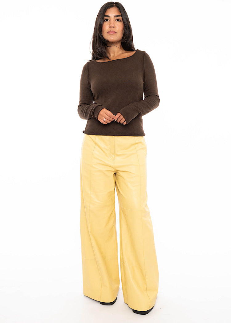 Model wearing Yellow wide leg leather trousers with a seam detail down the centre of the leg. Styled with brown fitted pullover with black high heels.