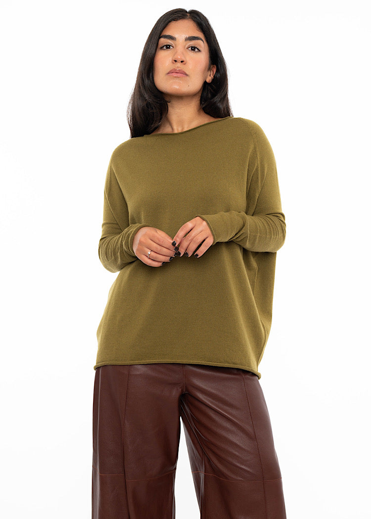 A Model wearing a relaxed fit khaki green pullover with a tight neckline and long gathering fitted sleeves. Showing the fitted areas of the pullover and the more relaxed areas .