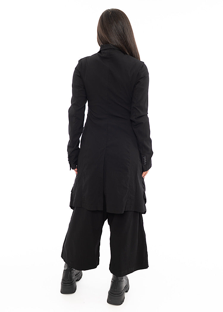 A Model facing the back wearing a detailed techno coat and matching trousers, in a Black colour. Showing the fitted look and the slight slit.