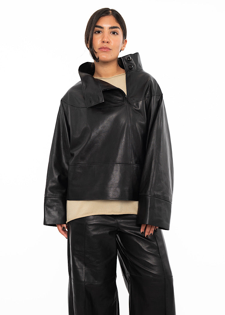 A model wearing an oversized Black Leather pullover with relaxed fit sleeves with a beige pullover underneath. Styled with wide leg trousers in the matching Black leather