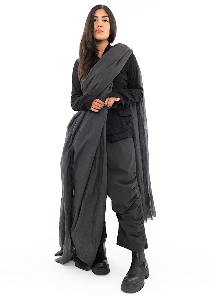 A full frame photo of A Model wearing an oversized long Washed Grey Scarf, styled wrapped over her with a Black Jacket and Black Boots.