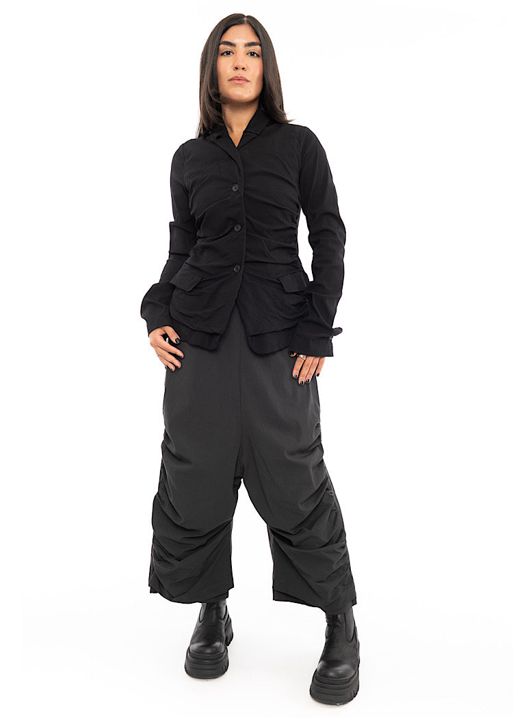 A full frame photo of A Model wearing a drop-crotch Trouser in a washed dark Grey colour. With a kick-flare leg and structured leg designs.