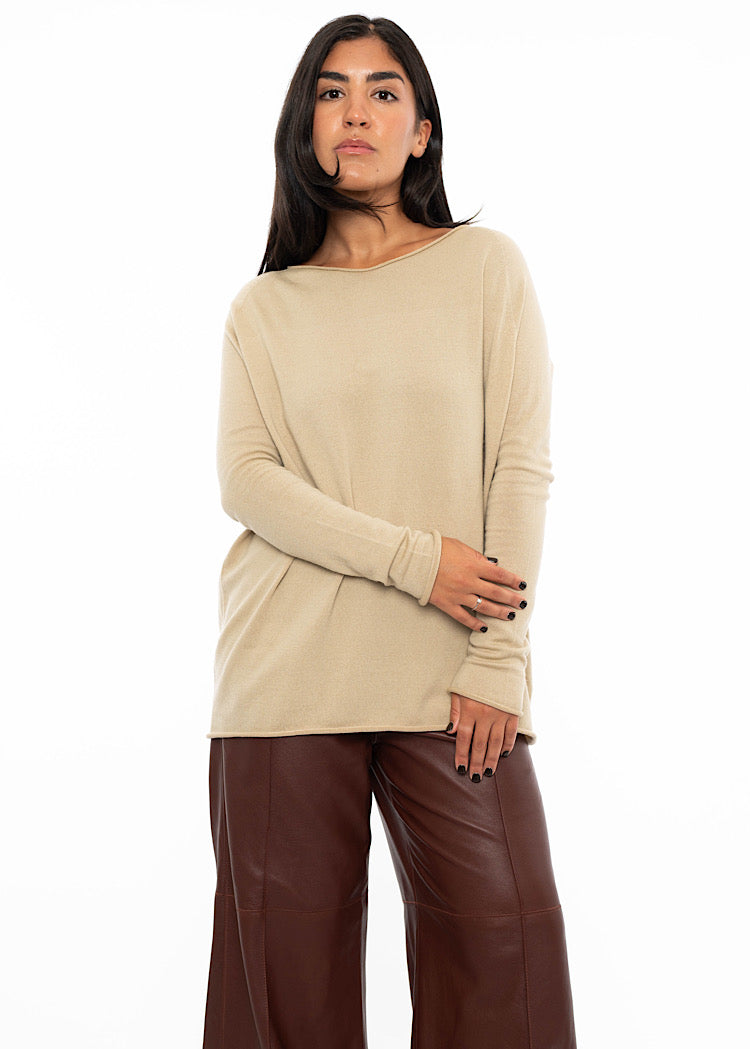 A Model wearing a relaxed fit creme pullover with a slash neckline and long sleeves, finishing at the hip. Styled with burgundy wide leg leather trousers.
