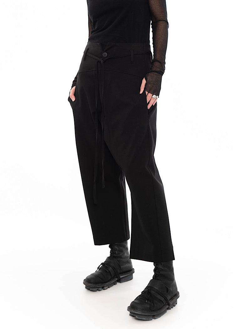 Model wearing black drop-crotch trousers with wide leg and drawstring detail, styled with mesh-sleeve top and combat boots.