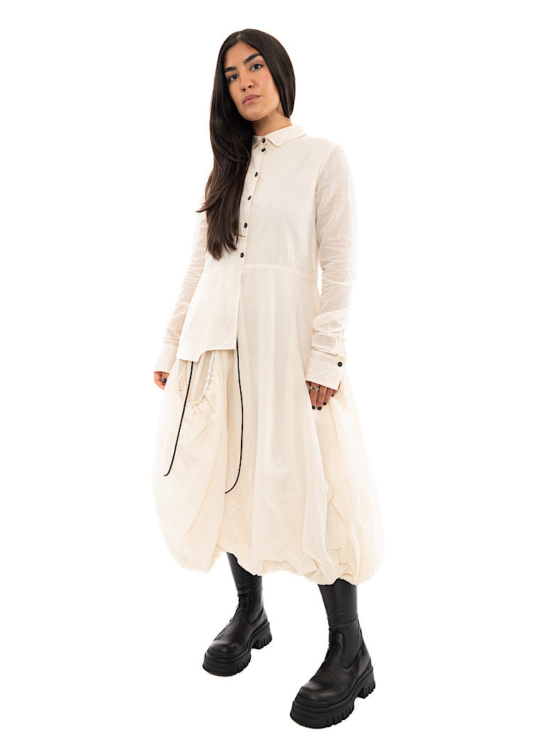 A full frame photo of A Model wearing a bubble skirted Dress in a creme colour. Focusing on the flap pocket and fitted sleeves.