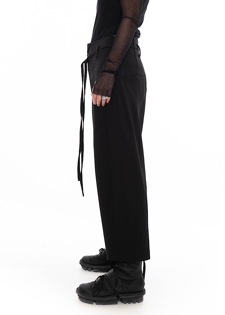 Side view of wearing black drop-crotch trousers with wide leg and drawstring detail, styled with mesh-sleeve top and combat boots.