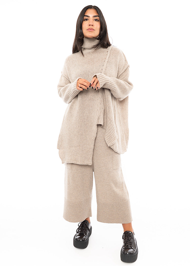 A full frame photo of A Model wearing a creme Knitted Pullover with Distressed pieces throughout. Showing the ribbed cuffs in more detail.