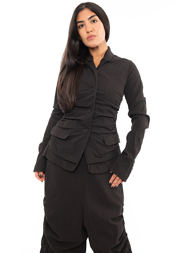 A Model wearing a detailed techno Jacket and matching trousers, in an off-Brown colour. Showing the matching suit together.