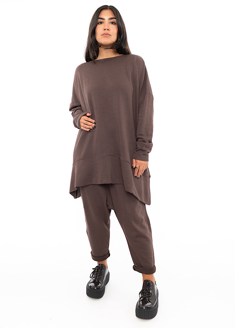 A full frame photo of A Model wearing a plum toned drop-crotch trouser. Paired with matching pullover and patent shoes.