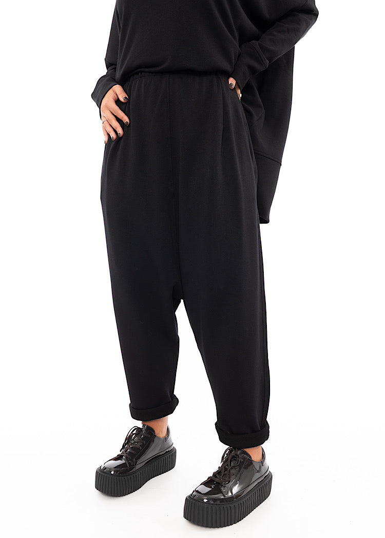 A Model wearing a Black Trouser with a slight rolled up ankle. Featuring slight seam details along the elasticised waistband.