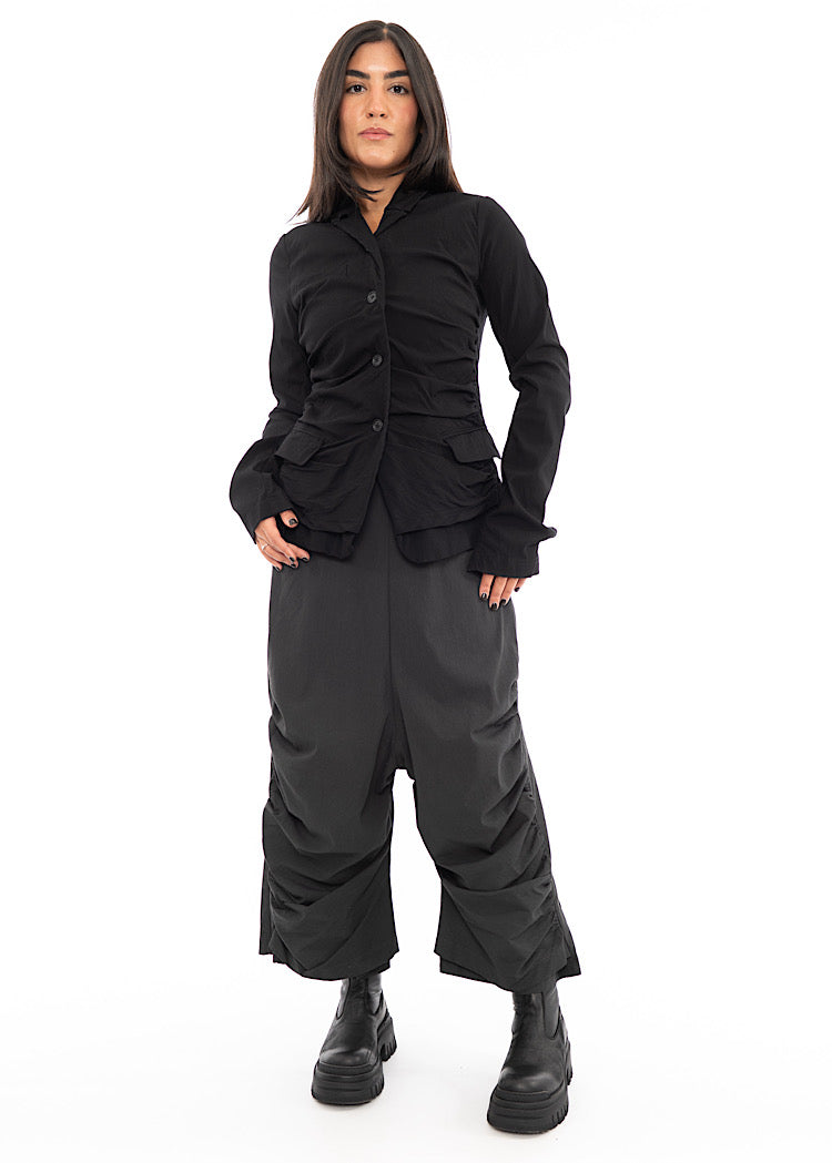 A full frame photo of A Model wearing a drop-crotch Trouser in a washed dark Grey colour. With a kick-flare leg and structured leg designs.