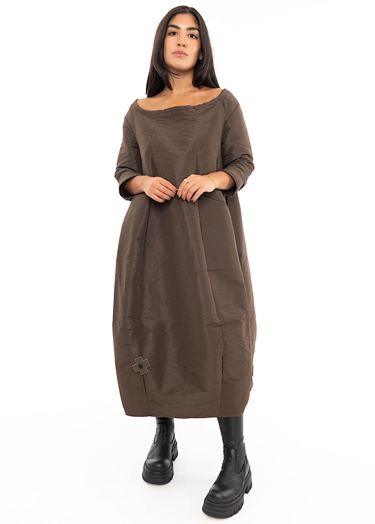 A Model wearing a structured balloon styled dress. Featuring a slash neckline, three-quarter length sleeves and side seam pockets.Styled with Black Boots.