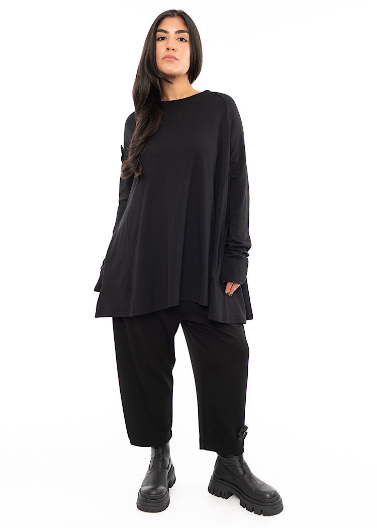 A full frame photo of A Model wearing a Black, oversized A-line top Styled with matching Black trousers and Chunky Boots.