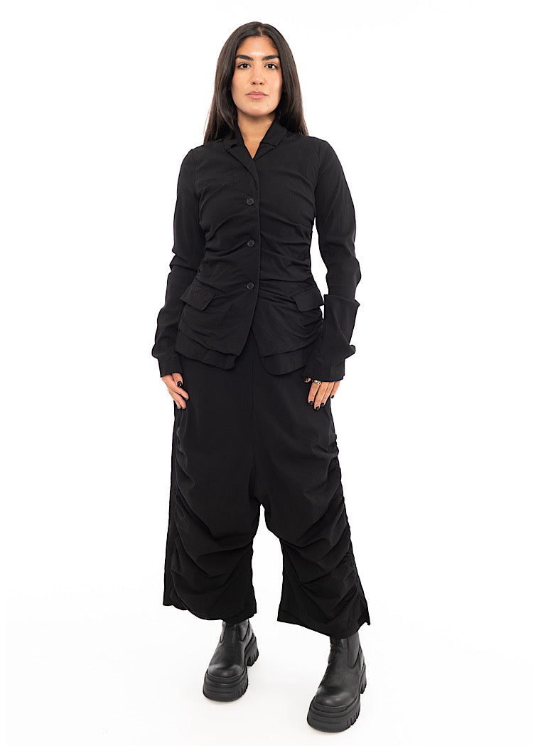 A full frame photo of A Model wearing a detailed techno Jacket and matching trousers, in a Black colour. Paired with a Black chunky boot.