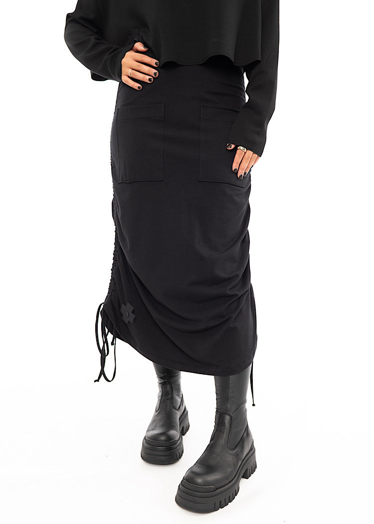 A Model wearing a Black drawstring Skirt, styled with a cropped Black Pullover and Chunky Black Boot.